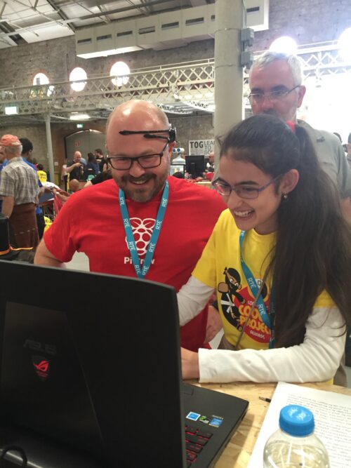 At a Coolest Projects event, a teenage girl tests out her mind-controlled robot at a laptop with a man.