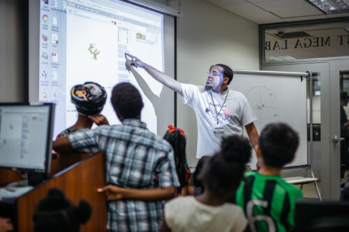 A mentor explains Scratch code using a projector in a coding club session.