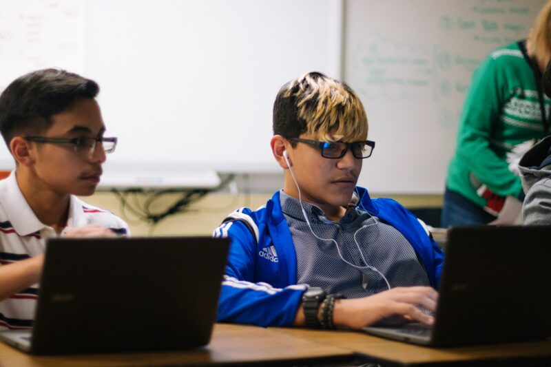Two boys at laptops in a classroom.