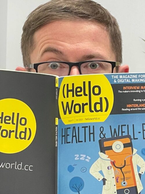 An educator holds up a copy of Hello World magazine in front of their face.